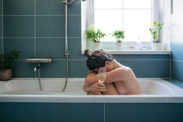 Depressed woman drinking wine in bathtub, is drunk. Young woman feeling hopeless, alcoholism issues in young age. Early alcohol abuse.