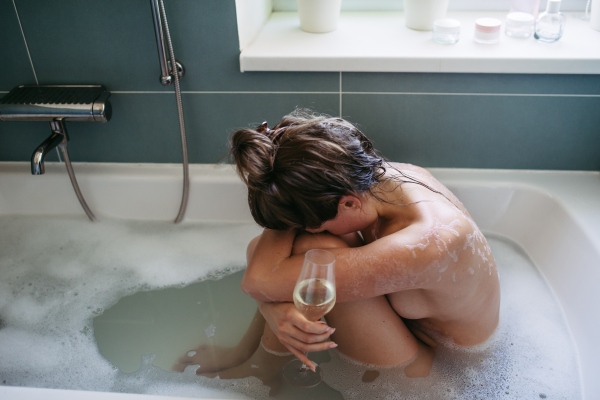 Depressed woman drinking wine in bathtub, is drunk. Young woman feeling hopeless, alcoholism issues in young age. Early alcohol abuse.