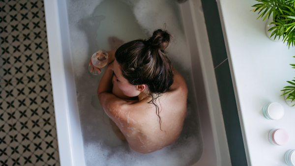 Depressed woman drinking wine in bathtub, is drunk. Young woman feeling hopeless, alcoholism issues in young age. Early alcohol abuse.