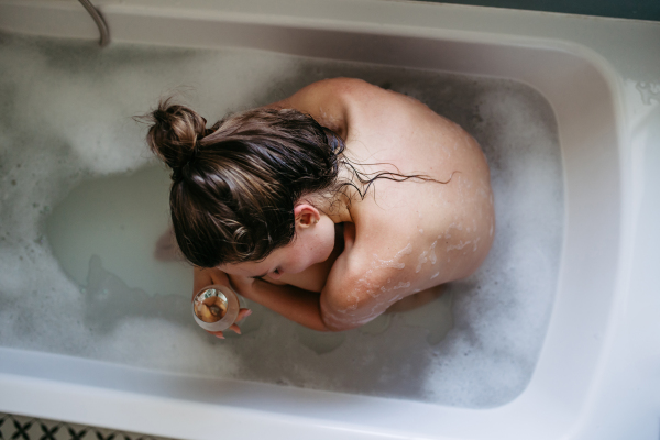 Depressed woman drinking wine in bathtub, is drunk. Young woman feeling hopeless, alcoholism issues in young age. Early alcohol abuse.