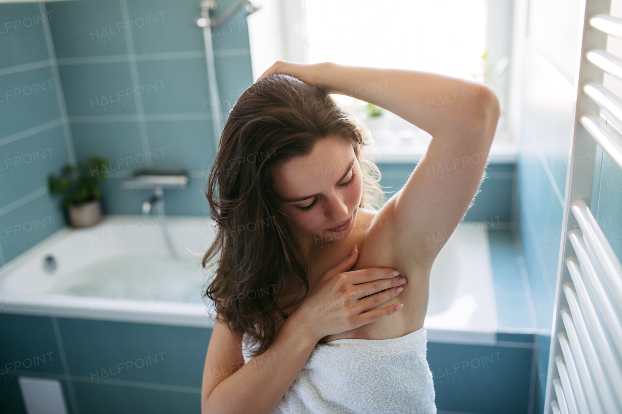 Breast self-exam at home. Yong woman standing in bathroom examining her brest, looking for lumps, breast cancer.