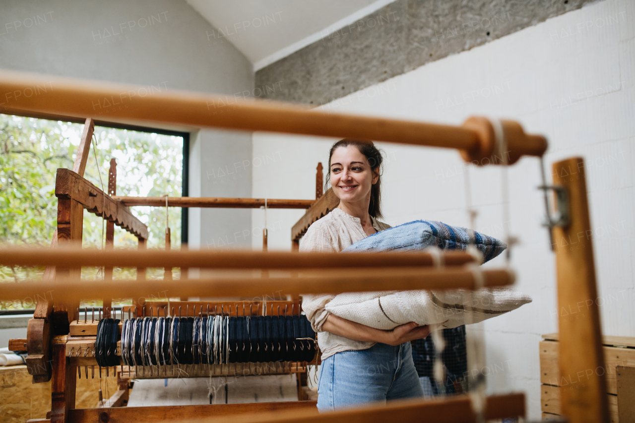 Young businesswoman next to wooden loom, holding pillows with woven covers made from recycled fabrics.. Upcycling in business and circular economy.