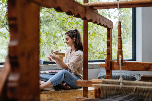 Businesswoman looking at swatch book, sitting by wooden loom. Upcycled textile, small cloth weaving business and circular economy.