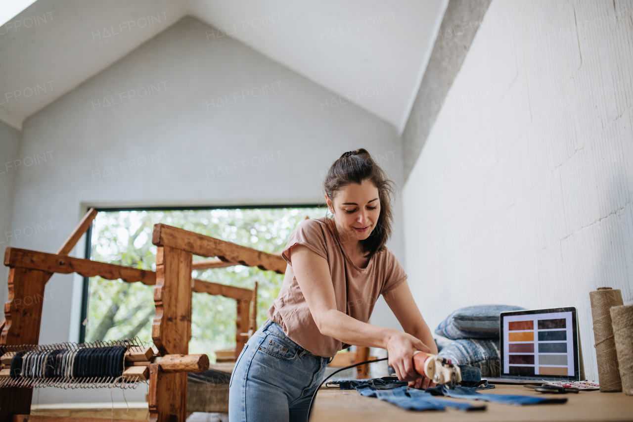 Young businesswoman working on workbench, preparing old fabric for weaving. Upcycled textile, small cloth weaving business and circular economy.