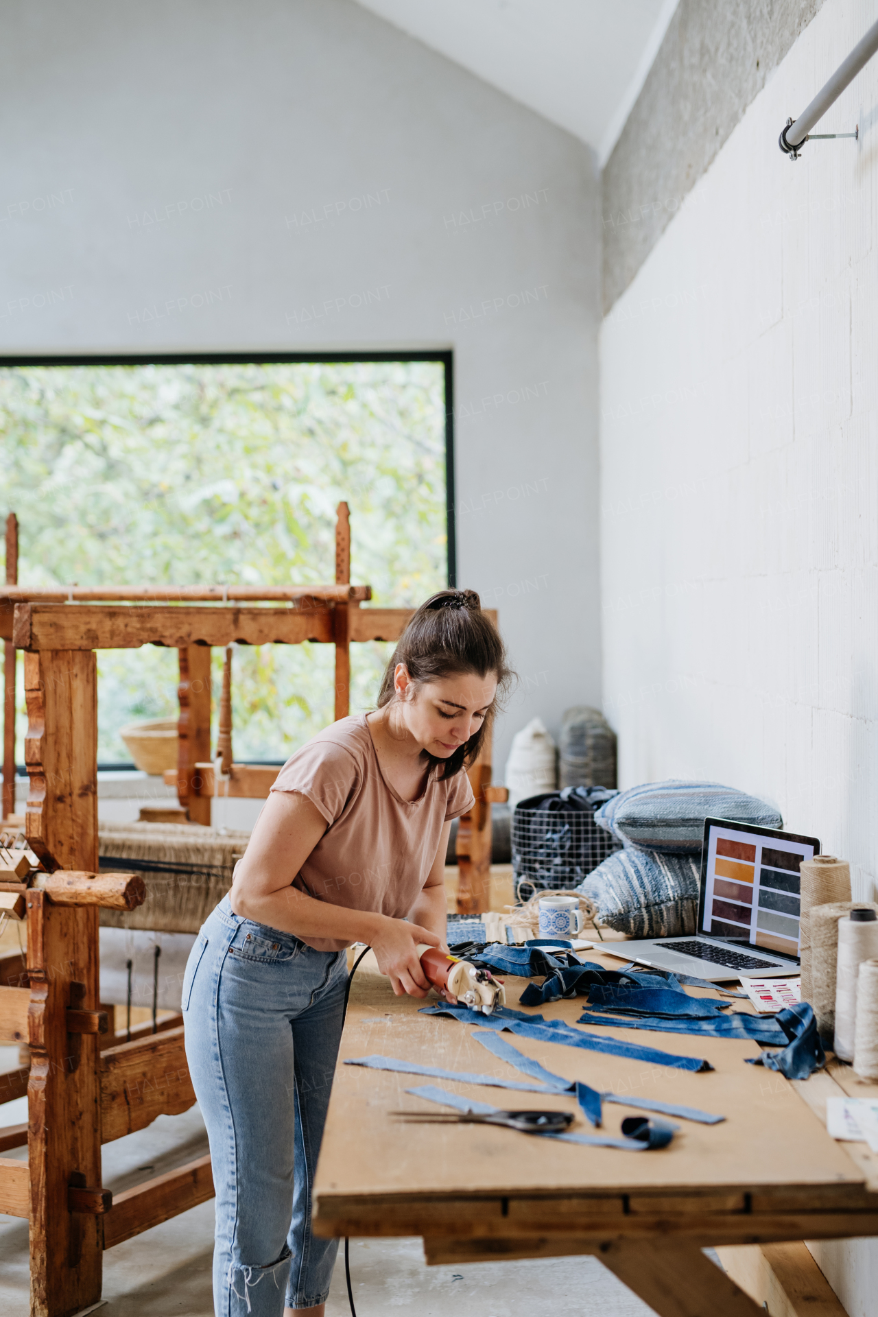 Young businesswoman working on workbench, preparing old fabric for weaving. Upcycled textile, small cloth weaving business and circular economy.