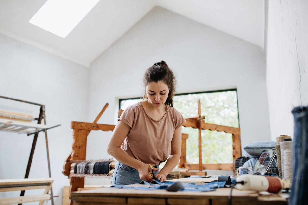 Young businesswoman working on workbench, preparing old fabric for weaving. Upcycled textile, small cloth weaving business and circular economy.