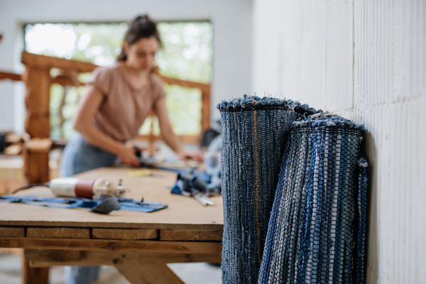 Young businesswoman working on workbench, preparing old fabric for weaving. Upcycled textile, small cloth weaving business and circular economy.