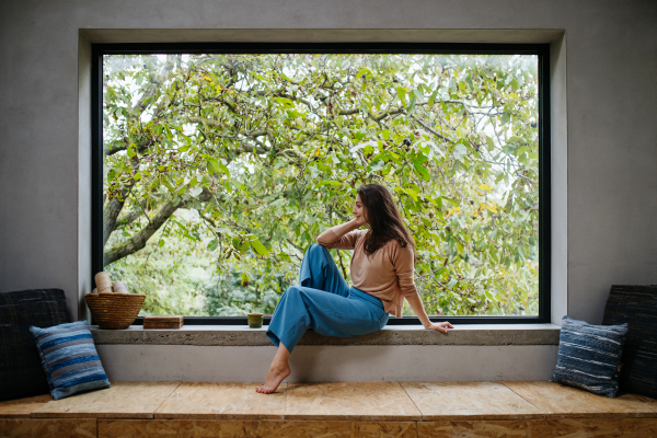 Beautiful woman sitting in front of large window, clean space