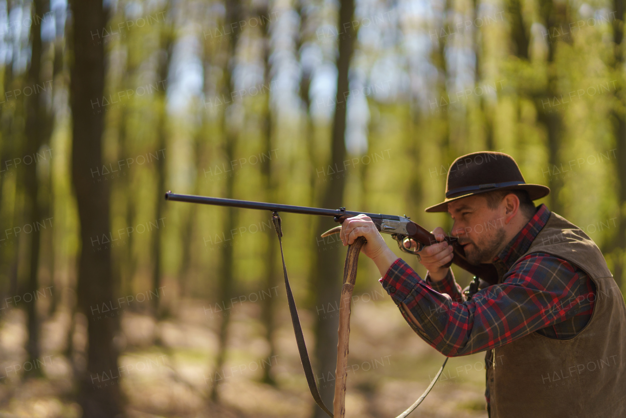 A hunter man aiming with rifle gun on prey in forest.