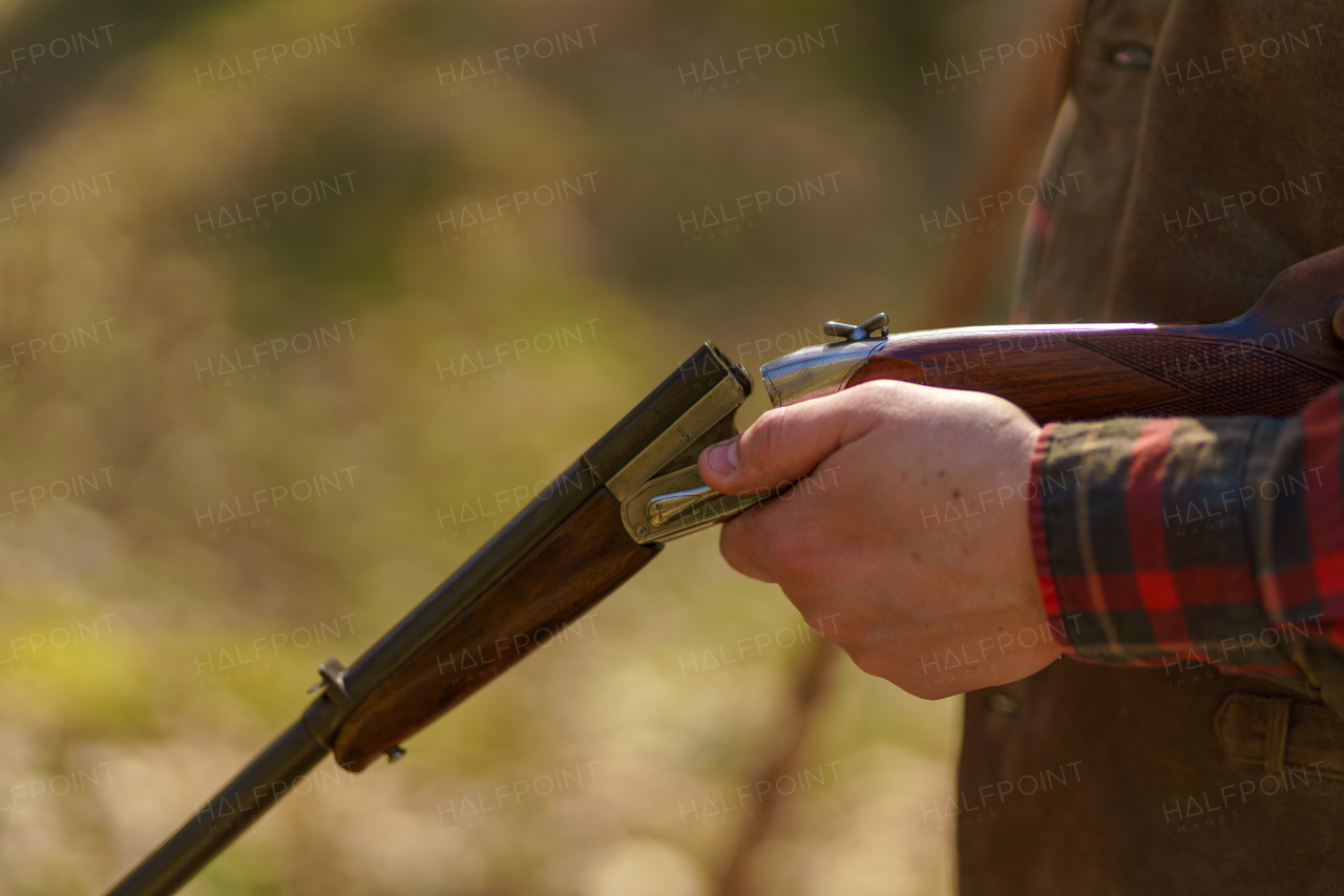 A close-up of hunter man charges the cartridge on rifle gun in forest.