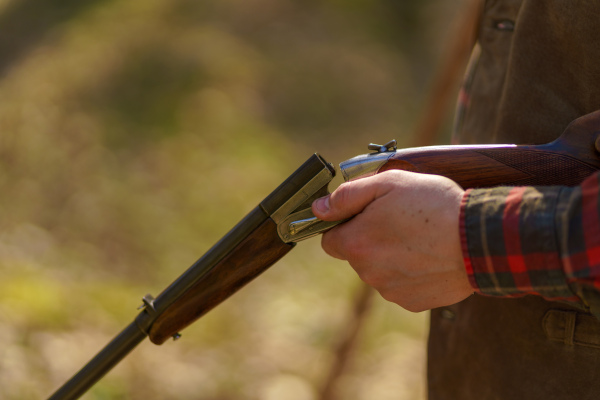 A close-up of hunter man charges the cartridge on rifle gun in forest.