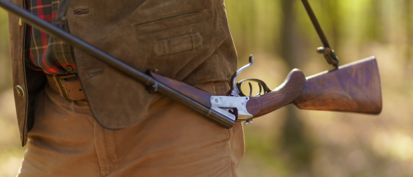 A close-up of hunter man carrying his rifle gun in forest.