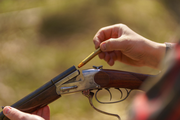 A close-up of hunter man charges the cartridge on rifle gun in forest.