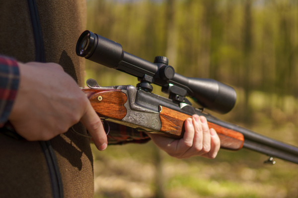 A close-up of hunter man waiting with rifle gun on prey in forest.