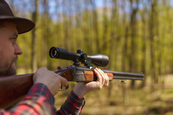 A hunter man aiming with rifle gun on prey in forest.