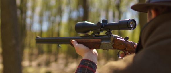 A hunter man aiming with rifle gun on prey in forest.