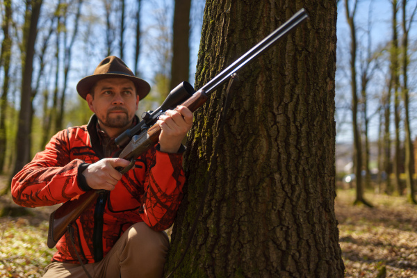 A hunter man with rifle gun waiting for prey in forest.