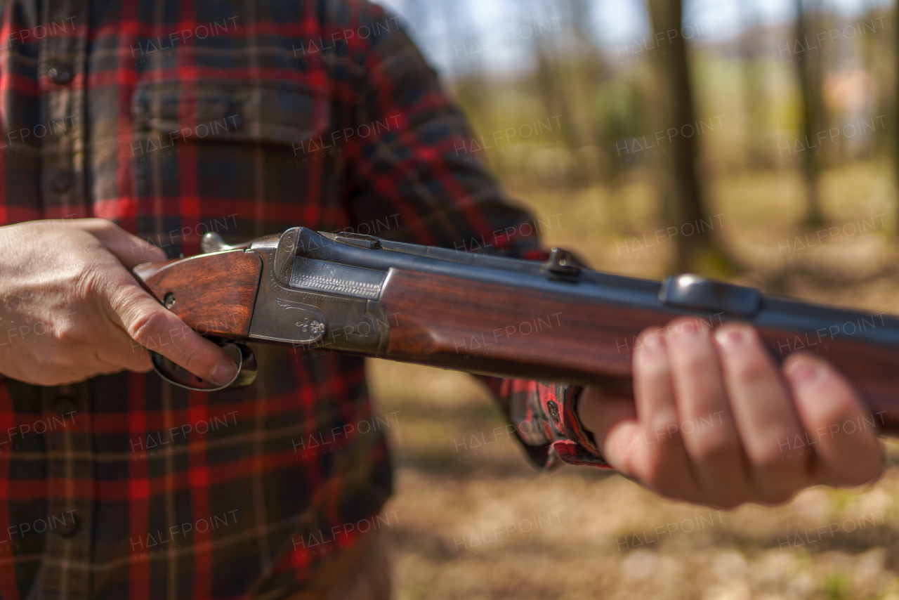 A close-up of hunter man charges the cartridge on rifle gun in forest.