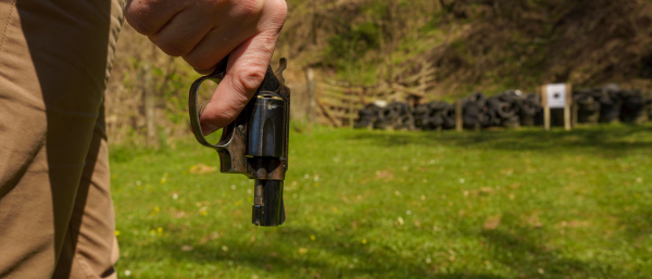 An unrecognizable man with revolver preparing to shot target on shooting range outdoors.