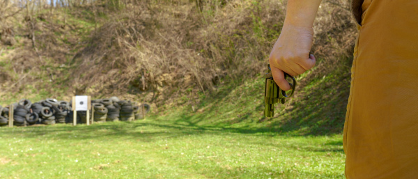 An unrecognizable man with revolver preparing to shot target on shooting range outdoors.