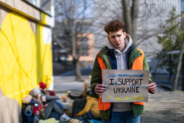 A protest against Russian invasion of Ukraine. Woman holding anti war banner near refugee camp.