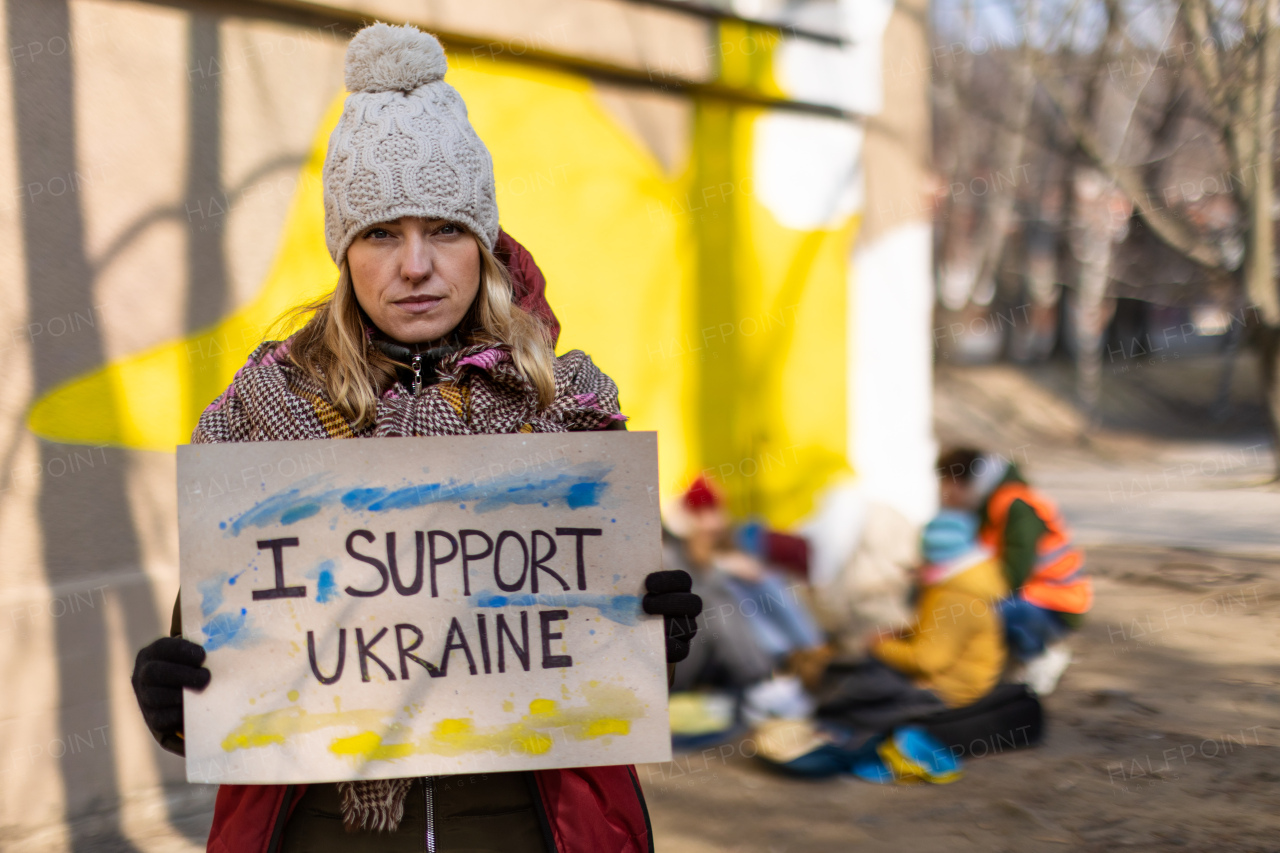 A protest against Russian invasion of Ukraine. Woman holding anti war banner near refugee camp.