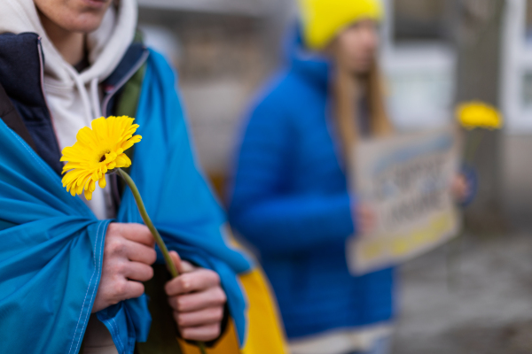 Protest against Russian invasion of Ukraine. A young woman wrapped in Ukrainian flag holding blue and yellow flowers.