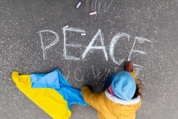 A top view of little girl writing peace with chalk. Protest against Russian invasion of Ukraine.