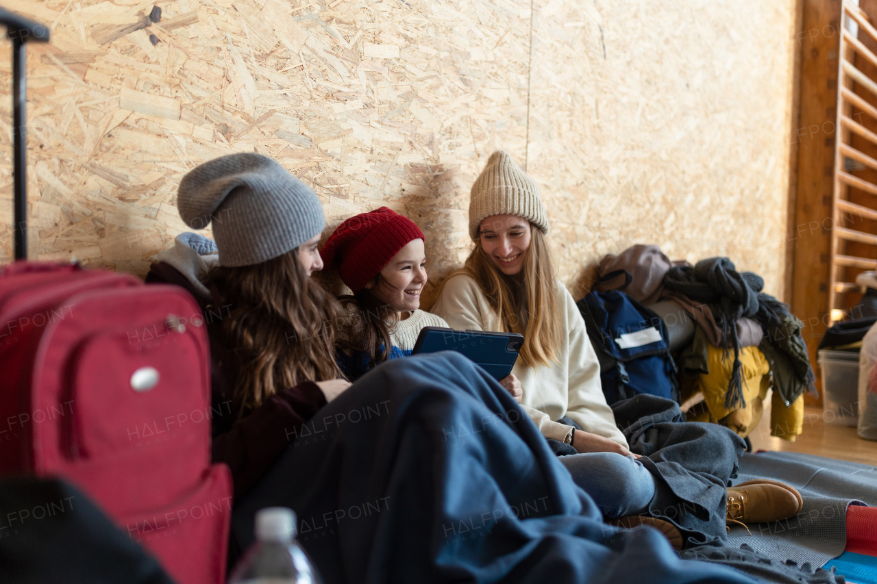 Happy Ukrainian war refugees in a temporary shelter and help center, using tablet.