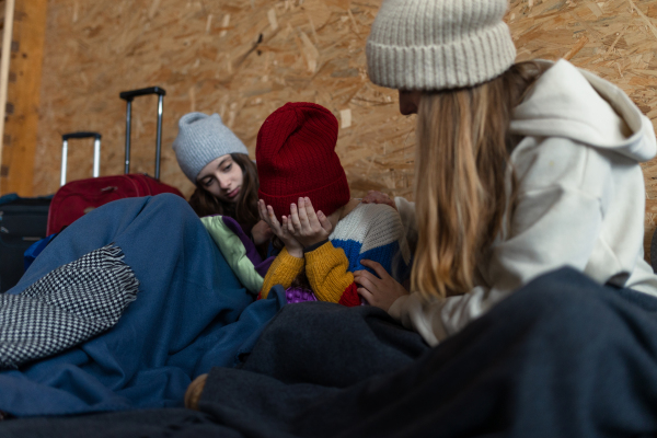 The Ukrainian war refugees in temporary shelter and help center, girls consoling little sad sister.