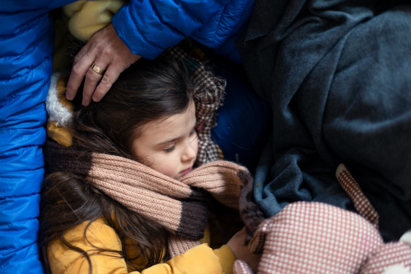 Ukrainian war refugees in temporary shelter and help center, a little girl sleeping on her mother's lap.