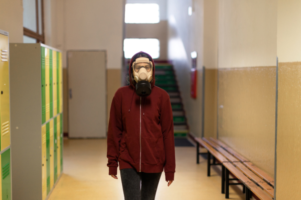 A young student in gas mask looking at camera at school.