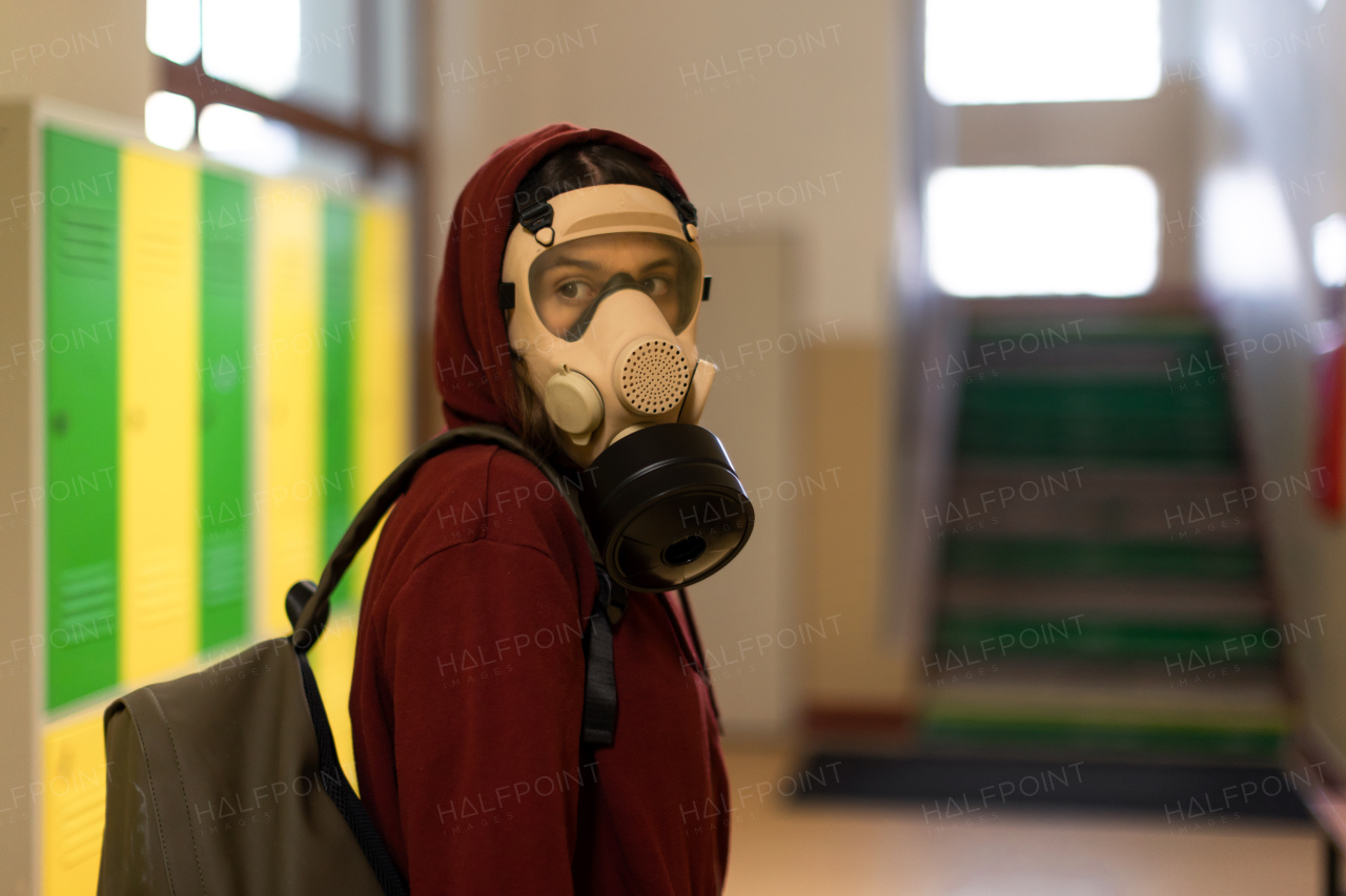 A young student in gas mask looking at camera at school.