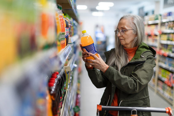 Elder senior woman buying and choosing flavoured water in supermarket.