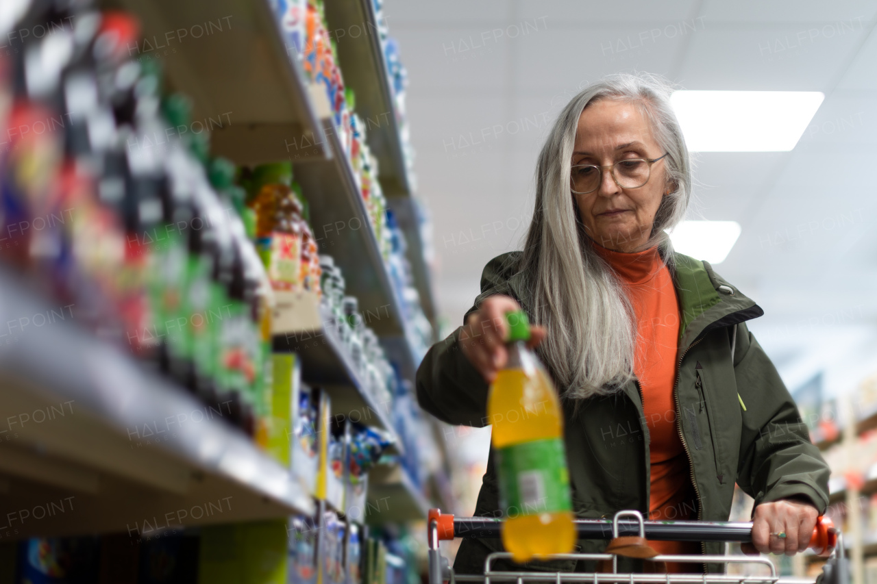 Elder senior woman buying and choosing flavoured water in supermarket.