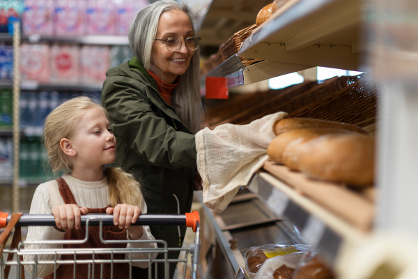 Grandmother with her granddaughter choosing and buying bread in supermarket.