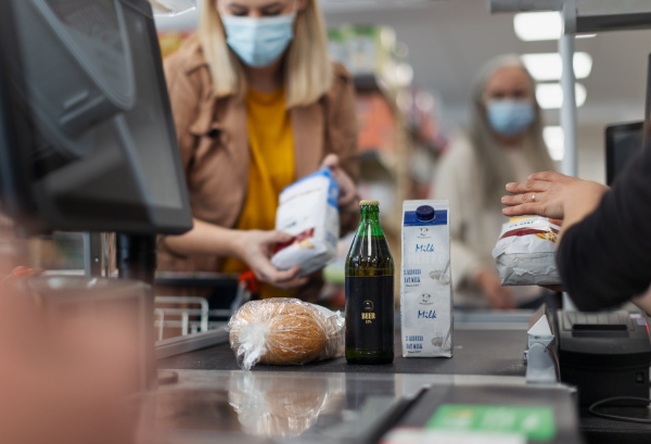 A young woman shopping in supermarket, putting products on checking desk during pandemic