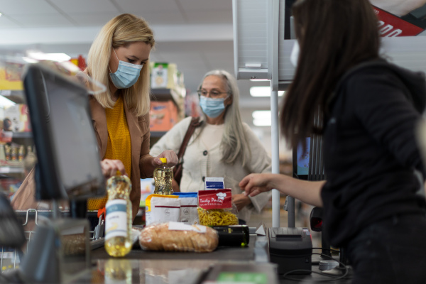 A young woman shopping in supermarket, putting products on checking desk during pandemic