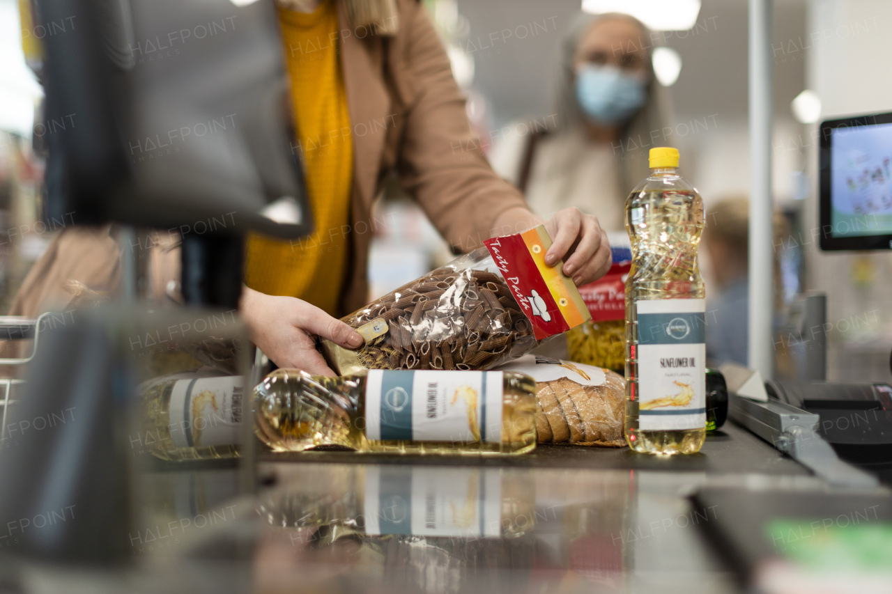 A cropped view of young woman shopping in supermarket, putting products on checking desk