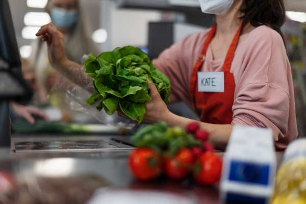 Checkout counter cashier scans vegetable in supermarket.