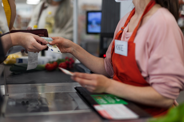 Cose-up of woman giving money to shop assistent in supermarket