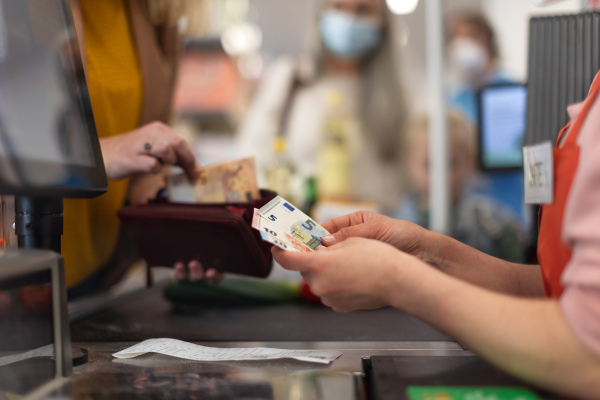 Cose-up of woman giving money to shop assistent in supermarket