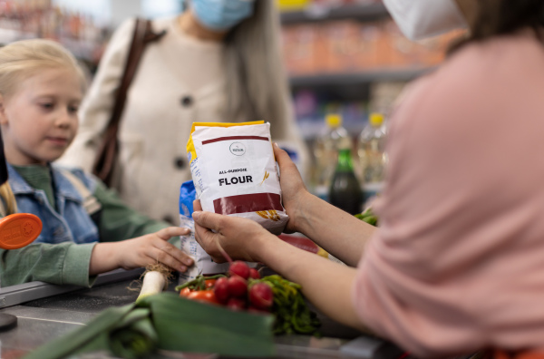 A little girl with mother shopping in supermarket, putting products on checking desk