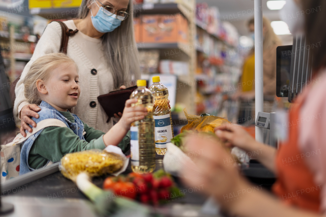 A grandmother with her little granddaughter shopping in supermarket, putting products on checking desk