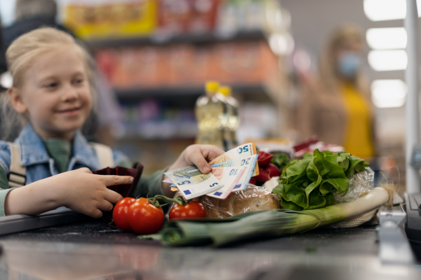 Close-up of a little blond girl paying for grocery shopping in supermarket.