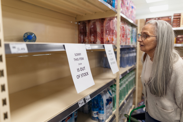 A depressed senior woman shopper in front of empty shelves in a grocery store