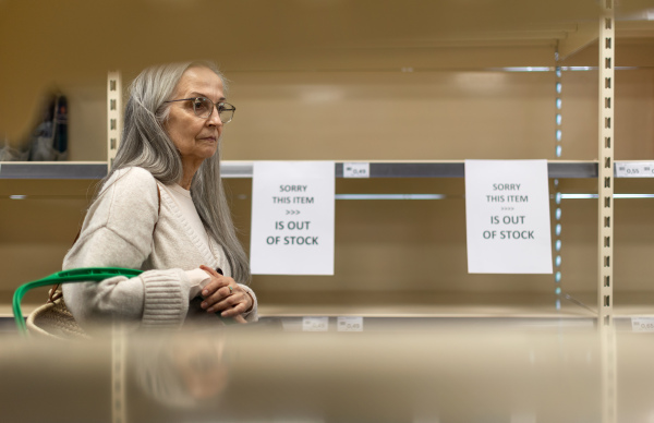 A depressed senior woman shopper in front of empty shelves in a grocery store