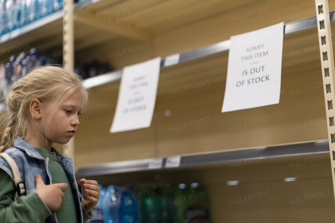 A little girl shopping and looking to empty shelves in a grocery store