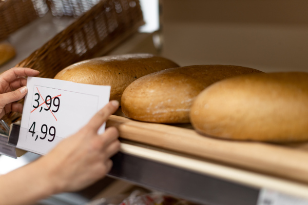 A woman shop assistant changing prices of bread in supermarket, the concept of increasing inflation