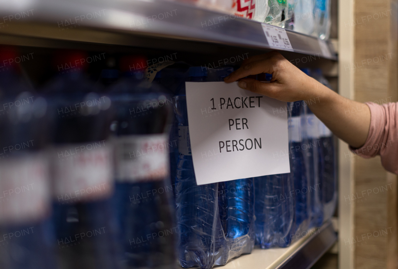 A woman is taking mineral water from superaket shelves, limited sales to one pack per person during coronavirus.